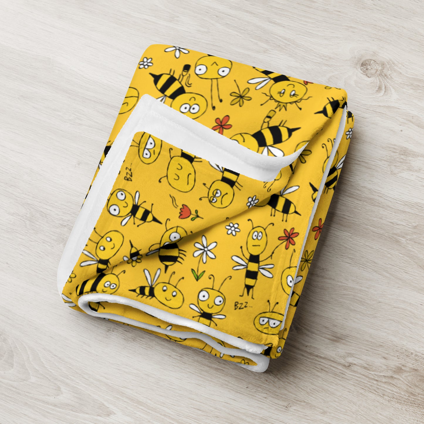 Folded yellow blanket with bee pattern on a light wooden surface