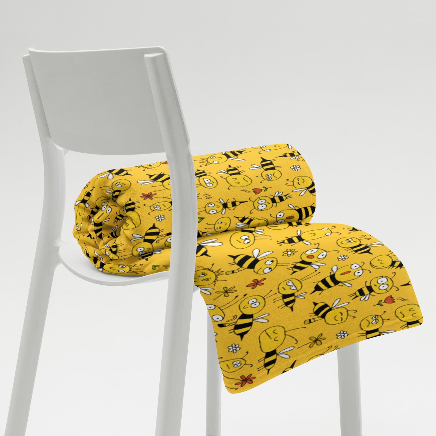 Yellow bee-patterned fabric rolled up on a white chair against a light gray background